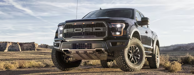 Powerful dark pickup truck with rugged tires on a desert terrain. The sun sets in the background, highlighting the truck's bold, robust design.