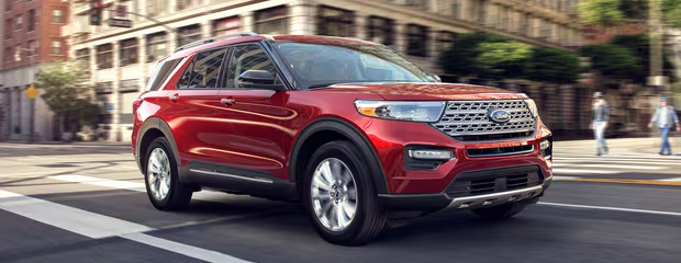 A shiny red SUV driving through a city street. The vehicle is in motion with blurred buildings in the background, conveying a sense of speed and urban life.