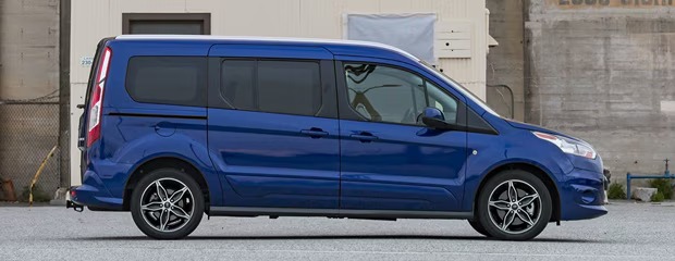 A sleek blue van is parked on a gray pavement in front of an industrial building. The van's modern design and shiny finish convey a sense of practicality and style.