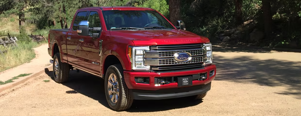 A shiny red pickup truck with chrome accents is parked on a dirt path, surrounded by green trees. The scene conveys power and adventure.