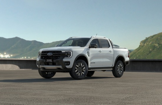 White pickup truck parked on a rooftop against a backdrop of green hills under a clear blue sky. The scene conveys a sense of adventure and ruggedness.