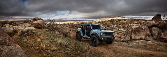 A blue SUV drives off-road on a rugged, rocky terrain under a cloudy, dramatic sky. The scene conveys adventure and rugged capability.