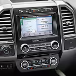 Close-up of a car infotainment system with a touchscreen display showing a navigation map. Surrounding buttons and air vents emphasize modern design.