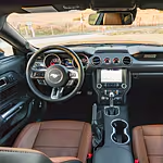 Interior view of a car showcasing a modern dashboard, leather seats, and a steering wheel with the Mustang logo. The ambiance is sleek and sophisticated.