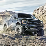 Black pickup truck driving through rugged, rocky terrain with dust clouds and hills in the background, conveying power and adventure.