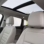 Interior of a car with beige leather seats and a panoramic sunroof, creating an airy and luxurious atmosphere, with trees visible through the glass.