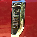 Close-up of a red vehicle's side badge, displaying "Platinum" and "F350" in chrome letters. The shiny metal adds a luxurious feel.