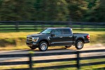 A black pickup truck speeds down a rural dirt road with a wooden fence and lush green trees in the background, conveying a sense of power and freedom.