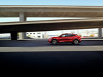 Red SUV driving on an urban highway under overpasses, with a clear blue sky above. The scene conveys a sense of speed and modern adventure.
