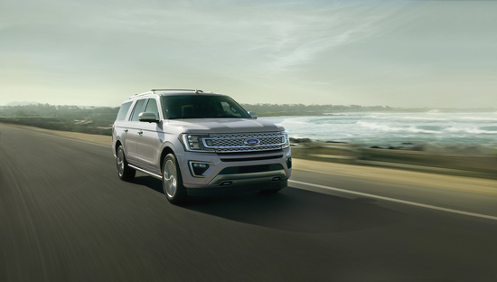 A silver SUV is driving along a coastal highway with waves crashing on the beach under a cloudy sky, conveying a sense of adventure and freedom.