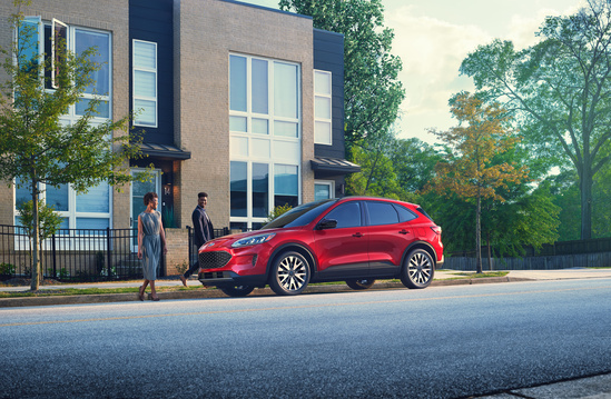 A sleek red SUV is parked on a sunny street, beside a modern building with metal accents and a green tree. The scene conveys a sense of urban elegance.