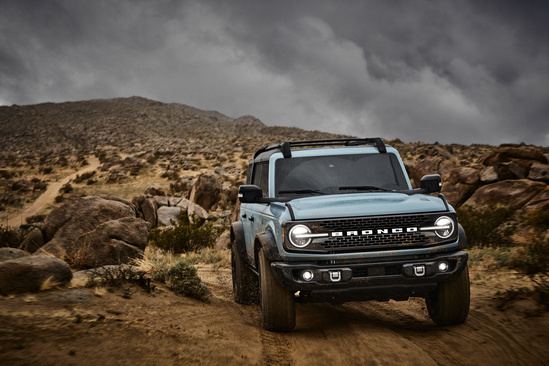 A rugged SUV navigates a rocky, barren landscape under a dramatic cloudy sky. The scene conveys adventure and exploration in a remote desert setting.